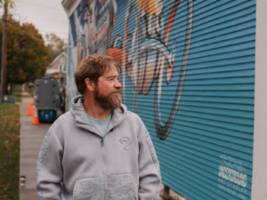 Artist Scott Takes, owner of Underground Art Studios, in front of his recently completed mural at Sacred Cow Tavern in Cedar Rapids, Iowa.